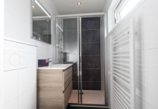 Baño moderno con ducha de vidrio, tocador de madera, espejo y ventana en De Thijmse Berg, Países Bajos.