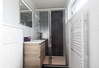 Baño moderno con ducha de vidrio, tocador de madera, espejo y ventana en De Thijmse Berg, Países Bajos.