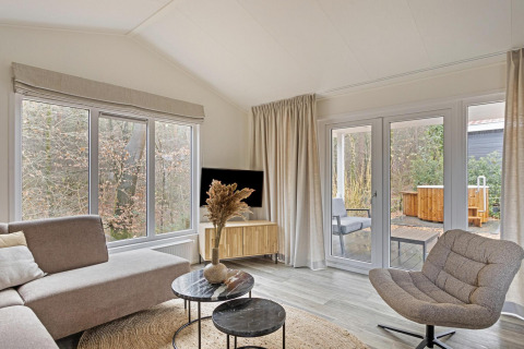 Salón luminoso y moderno en Wellness Lodge de De Thijmse Berg, Países Bajos, con amplios ventanales y decoración elegante.