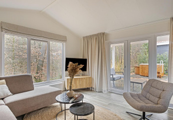 Salón luminoso y moderno en Wellness Lodge de De Thijmse Berg, Países Bajos, con amplios ventanales y decoración elegante.