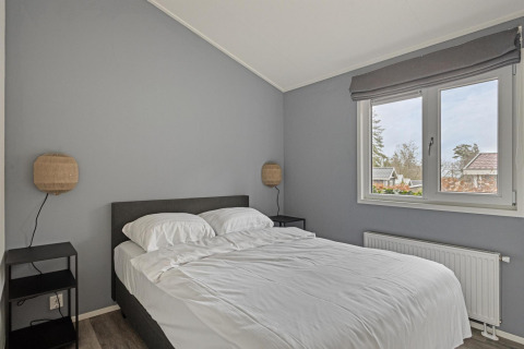 Dormitorio moderno con paredes grises, cama doble, ropa de cama blanca, mesillas y ventana grande en Wellness Lodge.