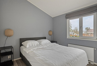 Camera moderna con pareti grigie, letto matrimoniale, biancheria bianca, comodini e ampia finestra al Wellness Lodge.