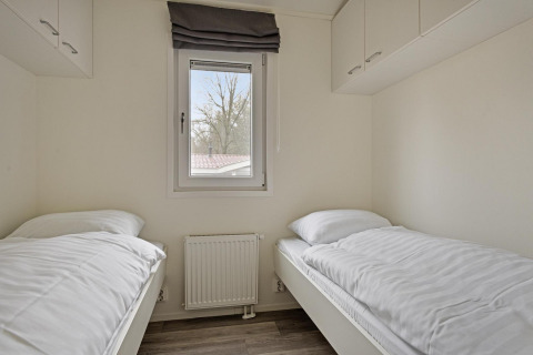 Slaapkamer met twee aparte bedden, een venster en opbergkasten in Wellness Lodge op De Thijmse Berg.