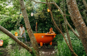 Coppia nel bosco, donna si rilassa in una vasca da bagno arancione a Les Cabanes d'Ostende, Belgio.
