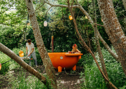 Stel in het bos, vrouw ontspant in oranje hottub bij Les Cabanes d'Ostende, België.