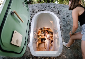 Donna che guarda in una piccola cantina sotterranea vicino a una tiny house, una donna sorride all'interno.