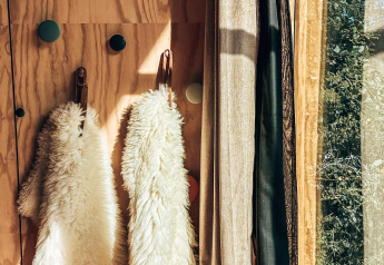 La luz del sol entra en la entrada de una tiny house con abrigos peludos colgados y cortinas.
