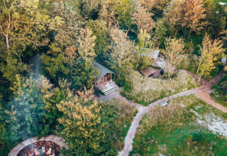 Aerial view of tiny houses surrounded by dense trees, winding paths, and a firepit seating area outdoors.