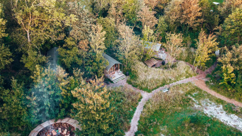Luchtfoto van kleine huisjes omgeven door bos, wandelpaadjes en een zitplek bij een open vuur.