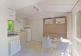 Lyst og moderne køkken og spiseområde i en hytte på Camping de Strasbourg, Frankrig, med udsigt til skov.