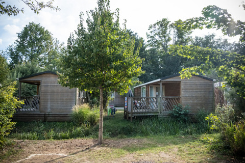 Dos cabañas móviles de madera entre vegetación en Camping de Strasbourg, Francia, un día soleado.