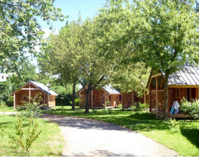 Sunny wooden cabins at Chalet Montana, Camping de l'Ill - Colmar in France, surrounded by green trees.
