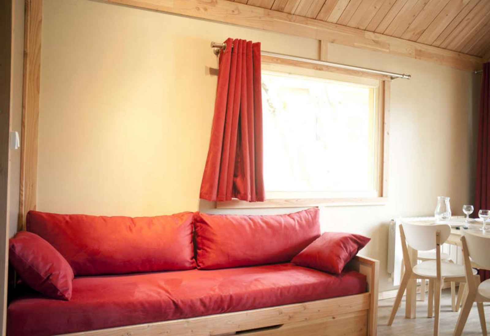 Licht houten interieur met rode bank en gordijnen in Chalet Montana, Camping de l'Ill - Colmar, Frankrijk.