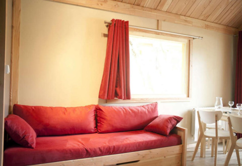 Interior de madera clara con sofá y cortinas rojas en el Chalet Montana, Camping de l'Ill - Colmar, Francia.