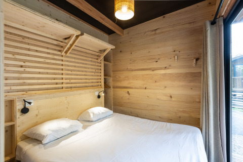 Dormitorio luminoso con paredes de madera y cama doble en Chalet Columbia, Camping de l'Ill - Colmar, Francia.