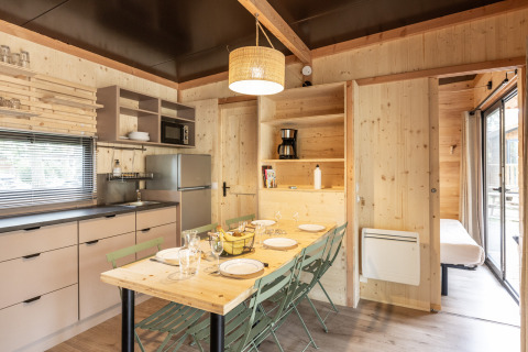 Interior de madera clara en la cabaña Chalet Columbia, cocina y mesa de comedor en Camping de l'Ill - Colmar, Francia.