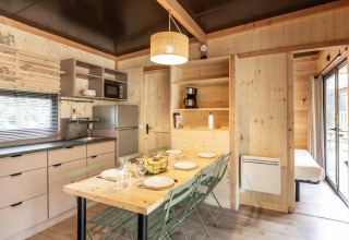 Interior de madera clara en la cabaña Chalet Columbia, cocina y mesa de comedor en Camping de l'Ill - Colmar, Francia.