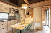 Interior de madera clara en la cabaña Chalet Columbia, cocina y mesa de comedor en Camping de l'Ill - Colmar, Francia.