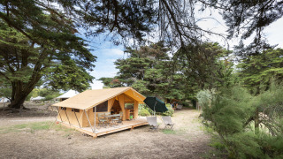 Das Safari-Zelt Tente Toile&Bois Classic steht auf einem Campingplatz, umgeben von hohen Bäumen.