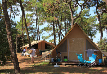 Tenda safari tra i pini all'Huttopia Noirmoutier, Francia, con sedie da campeggio e atmosfera familiare.