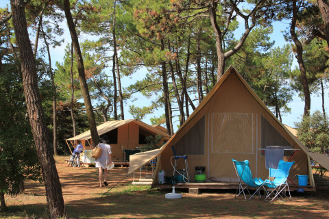 Safari-Zelte im Wald bei Huttopia Noirmoutier, Frankreich, mit Campingstühlen und entspannter Atmosphäre.