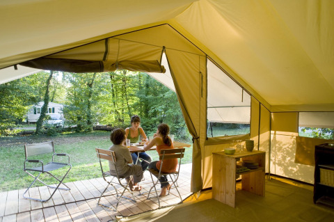 Vista interna di una tenda safari presso Huttopia Noirmoutier in Francia, con tre persone sedute a un tavolo nella natura.