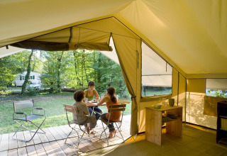 Indendørs udsigt fra en safari-telt hos Huttopia Noirmoutier i Frankrig, hvor tre personer sidder ved et bord i naturen.