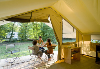Innenansicht eines Safarizelts bei Huttopia Noirmoutier in Frankreich mit drei Menschen am Tisch im Grünen.