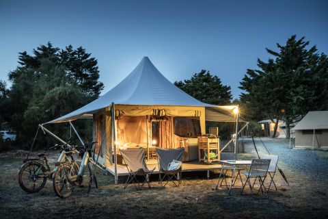 Panama Safari-Zelt mit beleuchtetem Eingang, Fahrrädern und Sitzbereich am Abend im Camp.