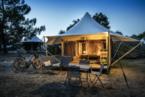 Tienda safari Panama Tent en Huttopia Ars-en-Ré, Francia, iluminada al anochecer con sillas y bicicletas afuera.