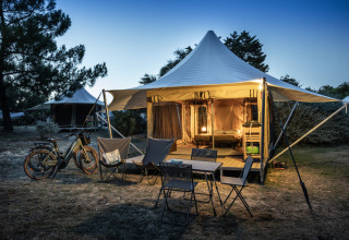 Tienda safari Panama Tent en Huttopia Ars-en-Ré, Francia, iluminada al anochecer con sillas y bicicletas afuera.