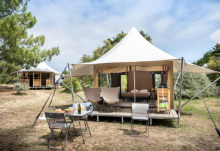Tienda safari Panama Tent en Huttopia Ars-en-Ré, Francia, con terraza, sillas y rodeada de árboles.