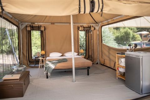 Interior de una tienda safari con cama, nevera y lámpara en Panama Tent de Huttopia Ars-en-Ré, Francia.