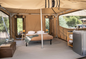 Innenansicht eines Safari-Zeltes mit Bett, Kühlschrank und Holzmöbeln im Panama Tent bei Huttopia Ars-en-Ré, Frankreich.