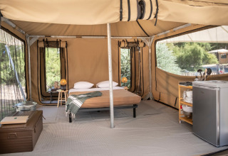 Interior of a safari tent with a bed, mini fridge, and lamp at Panama Tent in Huttopia Ars-en-Ré, France.
