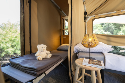 Binnenzicht van de Panama-tent in Huttopia Ars-en-Ré, Frankrijk met bedden, lampje en teddybeer.
