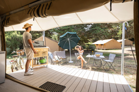 Koppel ontspant buiten een Panama safaritent bij Huttopia Ars-en-Ré, Frankrijk, op een campingterrein.