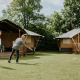 Two people play a lawn game in front of safari tents at Camping Si-Es-An in the Netherlands, surrounded by trees.