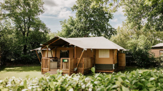Safaritent op Camping Si-Es-An in Nederland, omgeven door veel groen en bomen tijdens zonnig weer.