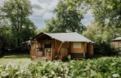 Tienda safari en Camping Si-Es-An, Países Bajos, rodeada de vegetación y árboles bajo un cielo azul.