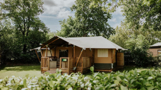 Safari-telt på Camping Si-Es-An i Holland, omgivet af grønne træer og buske under en blå himmel.