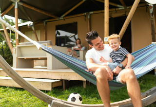 Vater und Sohn entspannen in einer Hängematte vor einem Safarizelt auf Camping Si-Es-An in den Niederlanden.