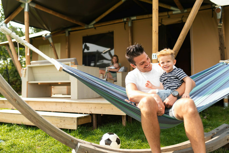 Padre e hijo disfrutando de una hamaca frente a una tienda safari en Camping Si-Es-An, Países Bajos.