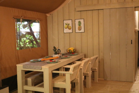 Eethoek in een safaritent op Camping Si-Es-An in Nederland, met houten tafel en stoelen.