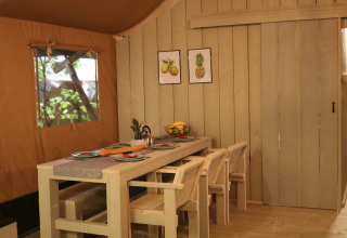 Indretning af spisestue i en safaritelte på Camping Si-Es-An, Holland, med træmøbler og vægkunst.