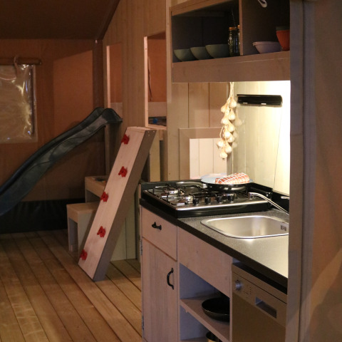 Interior de una tienda safari en Camping Si-Es-An, Países Bajos, con cocina y zona de juegos.