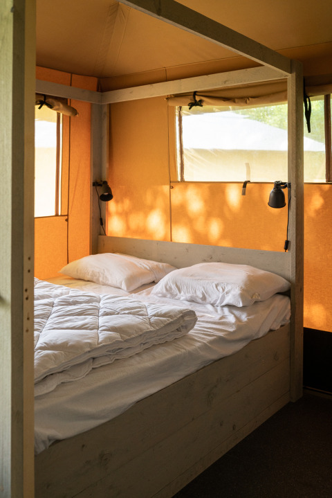 Interior view of a safari tent with a double bed at Camping Si-Es-An in the Netherlands, natural lighting.