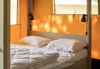 Vista interna di una tenda safari con letto matrimoniale al Camping Si-Es-An nei Paesi Bassi, luce naturale.