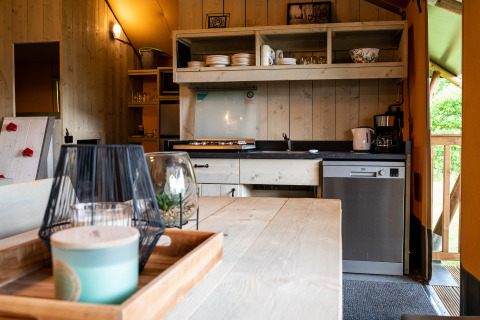 Interior view of a safari tent kitchen at Camping Si-Es-An with wooden table, dishes, and dishwasher.