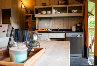 Interior view of a safari tent kitchen at Camping Si-Es-An with wooden table, dishes, and dishwasher.